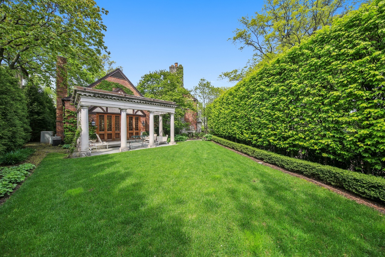 Finished backyard with manicured lawn, tall hedges, and a stone patio